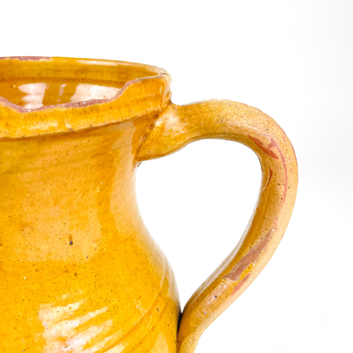 Late 19th century Spanish pottery pitcher from La Rioja, made in red earthenware and finished with a warm yellow glaze. The body displays wheel-turning marks, two shallow decorative bands, scattered glaze losses and firing variations, while the curved handle and shaped spout reflect the vessel’s original household function.