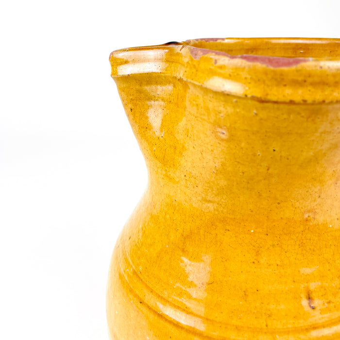 Antique yellow terracotta jug from La Rioja with a stable cylindrical base, softly rounded shoulder and narrowed upper body. Its handmade spout and large looping handle provide a confident utilitarian profile, while the ochre glaze varies from deep golden yellow to paler honey tones across the aged wheel-thrown surface.