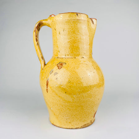 Antique Spanish terracotta jug in yellow glazed earthenware, sourced in Burgos, Castile, northern Spain. This 19th century pottery pitcher has a rounded body, straight neck, single strap handle, and pinched spout. The worn glaze and exposed clay suit Mediterranean decor, farmhouse decor, and rustic home decor.