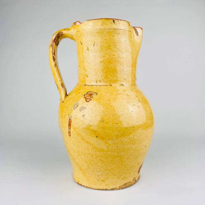 Antique Spanish terracotta jug in yellow glazed earthenware, sourced in Burgos, Castile, northern Spain. This 19th century pottery pitcher has a rounded body, straight neck, single strap handle, and pinched spout. The worn glaze and exposed clay suit Mediterranean decor, farmhouse decor, and rustic home decor.
