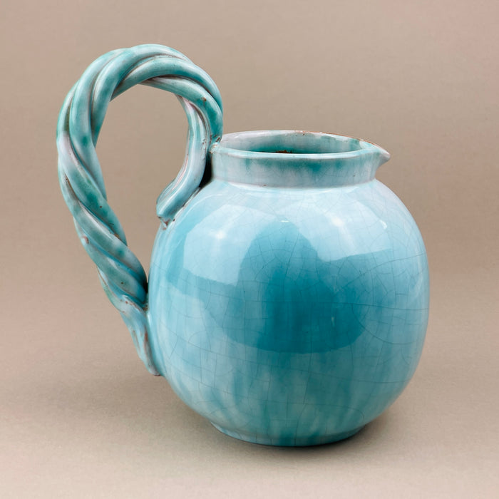 Blue ceramic pitcher with a twisted handle on a beige background. Side profile of the vintage Belgian jug attributed to Alexandre de Wemmel, showing the balanced proportions, rounded body, and spout detail. The turquoise glaze highlights the studio-crafted form, representative of 1950s mid-century European ceramics.