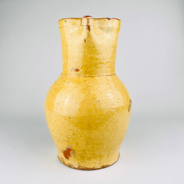 Spanish folk pottery jug in yellow glazed terracotta with a bulbous lower body and tall neck, dating to the 19th century. The handmade earthenware surface shows craquelure, firing variation, and age wear across the glaze. This antique Spanish pitcher works as a decorative vessel for Mediterranean decor and wabi sabi decor.