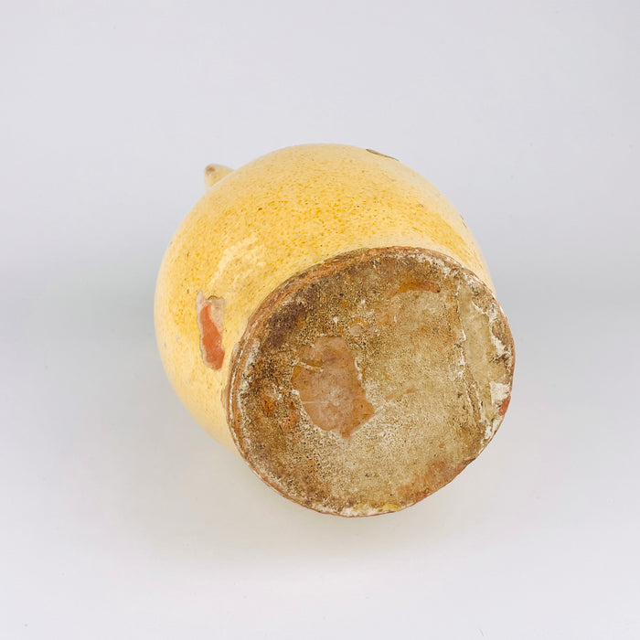 Spanish antique pitcher in yellow glazed terracotta with a rounded body and old-world rural profile, suited to display on a console, open shelf, or kitchen dresser. The glaze variation, craquelure, and exposed terracotta areas create the layered surface buyers seek in antique and vintage pottery for rustic home decor and Spanish interiors.
