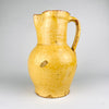 Nineteenth century Spanish terracotta jug with ochre yellow glaze, showing the rounded profile and narrow upper section typical of rural earthenware pottery. The vessel has surface losses and worn edges that reveal the red clay body beneath, giving it strong antique character for Mediterranean decor and antique kitchen pottery displays.