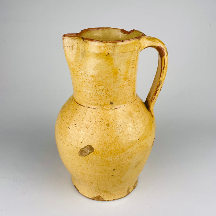Detail of the antique Spanish earthenware jug showing the weathered yellow glaze and exposed terracotta where age and handling have worn through the surface. This old pottery pitcher has the material honesty collectors look for in Spanish folk ceramics and suits wabi sabi decor, farmhouse decor, and curated rustic shelf styling.