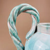 Close-up of a ceramic pitcher with a twisted handle on a beige background. Focus on the twisted rope handle, demonstrating the sculptural craftsmanship of Alexandre de Wemmel. This bold handle is a recurring motif in his mid-century ceramics, celebrated for merging utility with strong artistic expression.