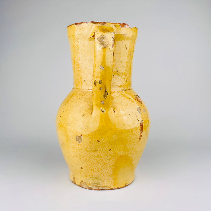 Antique Spanish pottery pitcher with a single applied handle and pinched pouring lip, made from terracotta and covered in a mellow yellow glaze. Sourced in Burgos, Castile, this 19th century jug has a practical rural form and visible wear that make it ideal as decorative pottery for Mediterranean decor and old kitchen vessel collections.