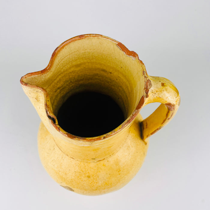 Detail highlighting the rim wear and interior of this antique Spanish terracotta jug, where chips, glaze losses, and age marks show the red clay body beneath the yellow finish. These visible imperfections support its old farmhouse pottery character and make it especially suitable for collectors of authentic Spanish earthenware and rustic decor.