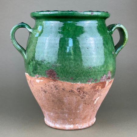 Ceramic vase with green top and brown bottom on a gray background. Side view of a vintage French terracotta confit jar with green glaze, highlighting the form’s classic proportions and smooth texture. The contrast between the natural clay and glazed surface enhances its appeal as an authentic farmhouse or wabi-sabi decorative vessel.