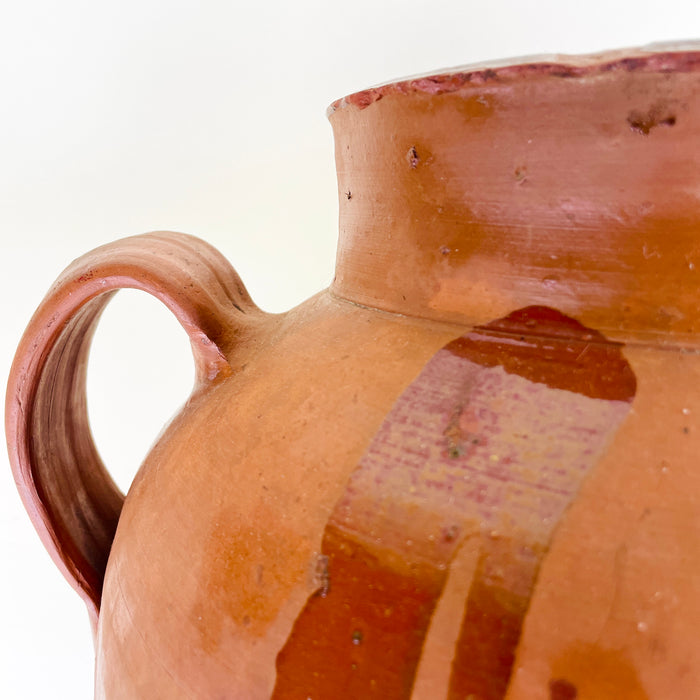 XL terracotta vase from early 20th century Spain, formed with two side handles, a broad shoulder, tapered base, and warm glazed surface showing scuffs, mineral residue, and handmade irregularities. This antique pottery vessel is suited to Mediterranean decor, Spanish farmhouse decor, and interiors using large clay objects.