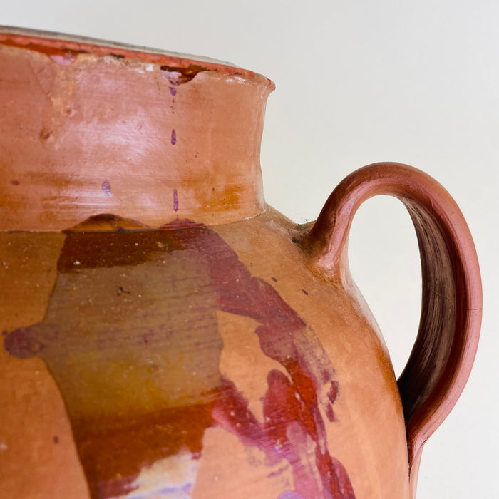 Spanish orza style terracotta jar with two handles, a heavy handmade body, amber glaze pooling, reddish brown drips, and an unglazed worn base showing long functional use. The antique pottery piece can be styled as a large floor vase, decorative storage jar, or rustic terracotta vessel for farmhouse decor.