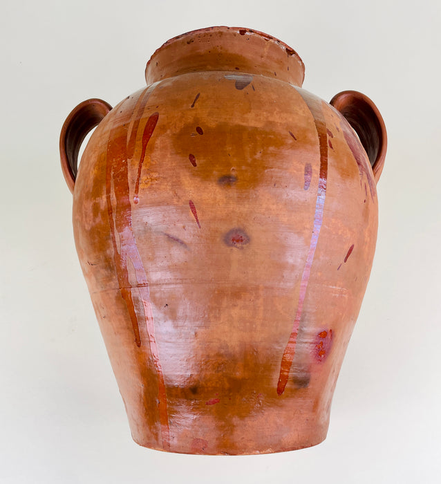 Antique Spanish terracotta jar with two handles and a wide mouth, showing amber glaze runs, reddish brown surface marks, handmade asymmetry, and age-related wear from long use. This large clay vessel supports search terms such as terracotta vase, Spanish pottery, antique vase, floor vase, and rustic farmhouse decor.