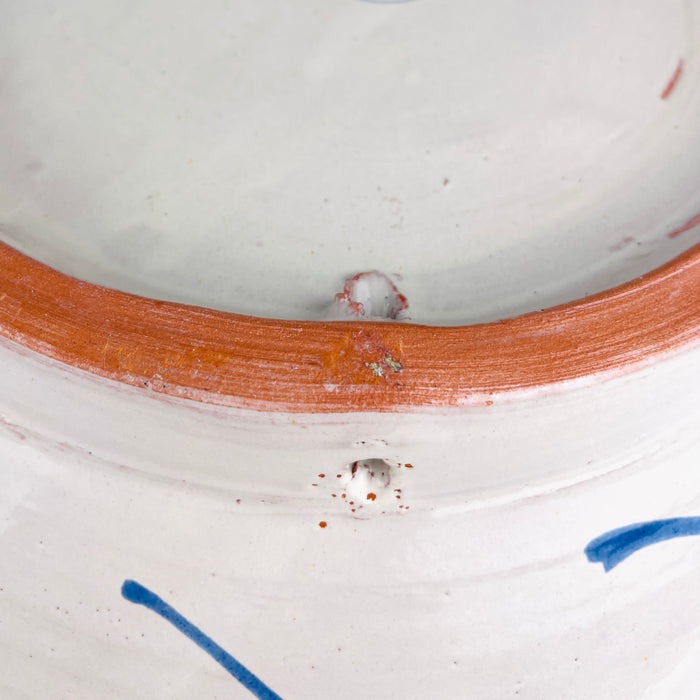 A ceramic vessel with a white glazed interior and exterior featuring a terracotta-coloured rim. The exterior surface displays hand-painted blue linear accents and small circular perforations near the top edge of the clay body.