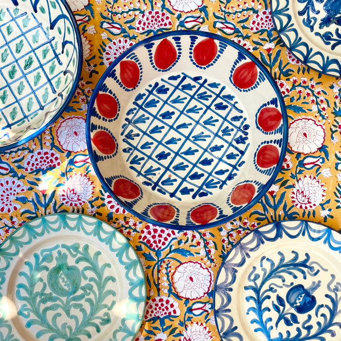 Hand painted Granada Fajalauza lebrillo bowl with a blue rim, red pomegranate border, and central blue lattice pattern on a cream glazed terracotta body. This contemporary Spanish pottery piece can be used as a decorative bowl, sculptural table centerpiece, or wall hanging ceramic in farmhouse decor and rustic home decor settings.