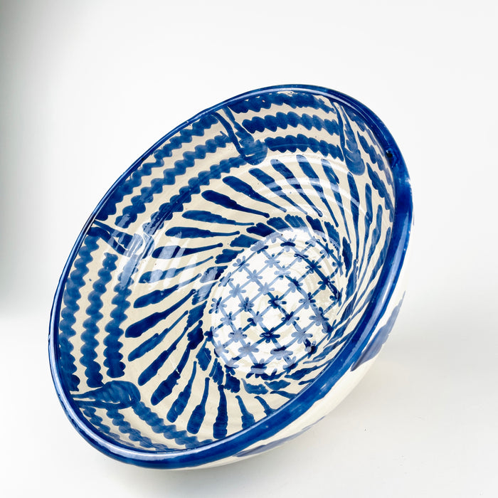 Decorated center of the Granada lebrillo bowl, featuring a cobalt blue crosshatched lattice punctuated by small flower-like brush marks and surrounded by radiating leaf forms. The expressive freehand pattern gives this large Spanish serving bowl a graphic focal point when displayed as ceramic wall art, a table centerpiece or a decorative bowl.