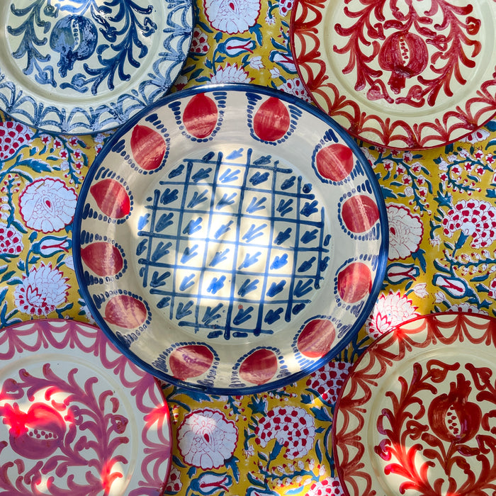 Red and blue Spanish Fajalauza lebrillo bowl designed by ROC Objects and produced in Granada in the traditional Fajalauza style. The piece combines a cream glazed interior, blue painted rim, red pomegranate motifs, and hand painted lattice pattern for use as a decorative bowl, wall hanging ceramic, or Mediterranean table centerpiece.