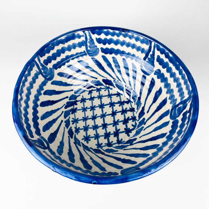 Large blue and white Granada lebrillo bowl with a spiral interior composition of cobalt leaf forms, wavy border bands and a central floral lattice. The traditional terracotta serving bowl has a substantial depth and footed base, while pierced holes near the rim allow it to function as a ceramic wall hanging or decorative wall plate.