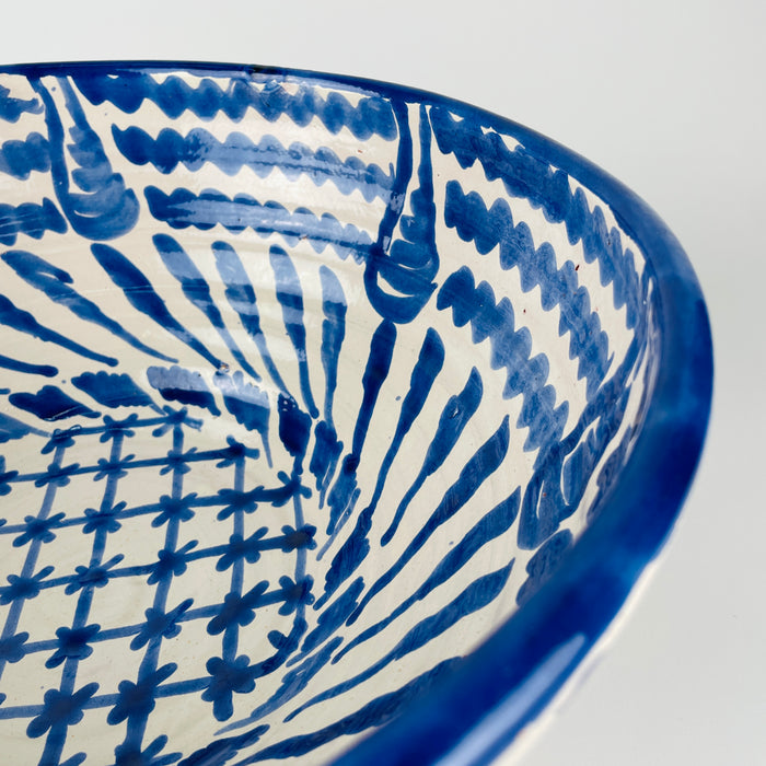 Exterior of the Granada lebrillo bowl with broad cobalt blue brush motifs sweeping across the white glaze above the exposed terracotta foot. Natural pitting, glaze variation and minor surface wear remain visible, reinforcing the handmade character of this substantial Spanish pottery serving bowl and decorative Mediterranean ceramic.