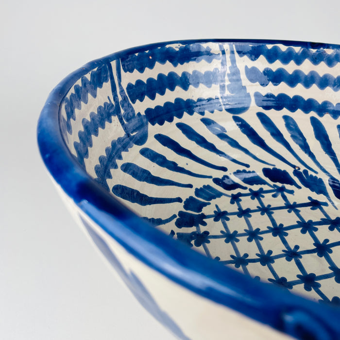 Blue and white interior pattern on a handcrafted terracotta bowl from Granada, arranged in a dynamic spiral around a central floral grid. The uneven freehand spacing, shifting cobalt tones and glossy white glaze give the Spanish Fajalauza lebrillo its individual character, complementing Mediterranean decor, farmhouse decor and eclectic wall displays.