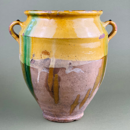Multicolored ceramic vase with handles on a gray background. Antique French terracotta confit pot with twin handles photographed front-facing, showing yellow and green drip glaze against unglazed lower clay. Ideal for French farmhouse decor, rustic Mediterranean kitchens, or as a sculptural statement in interior styling.