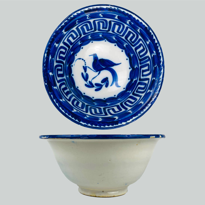 Antique Spanish Manises ceramic deep bowl in blue and white tin glazed earthenware from the Valencia region, featuring a hand painted cobalt bird in the center with a curling leafy branch. The rim is structured with a Greek key border and bold cobalt brushwork, ideal for Mediterranean decor styling and blue white kitchen decor or wabi sabi decor