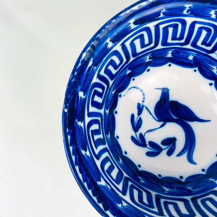 Antique Manises bowl from Spain in white tin glazed earthenware, featuring cobalt blue hand painted decoration with a bird motif and curling plant forms. The border includes a Greek key pattern and deep cobalt brushwork around the rim, ideal for a table centerpiece, decorative bowl display, or blue white ceramic accent in rustic home decor and coastal decor.