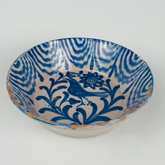 Antique Granada Fajalauza bowl made from tin glazed earthenware, decorated in cobalt blue with a bird and floral motif. The interior rim shows repeating wave bands and drip marks that create a bold border against the ivory glaze. Suitable for Spanish tableware, serving olives, citrus, or salads, and for Mediterranean decor shelves with collected ceramics.