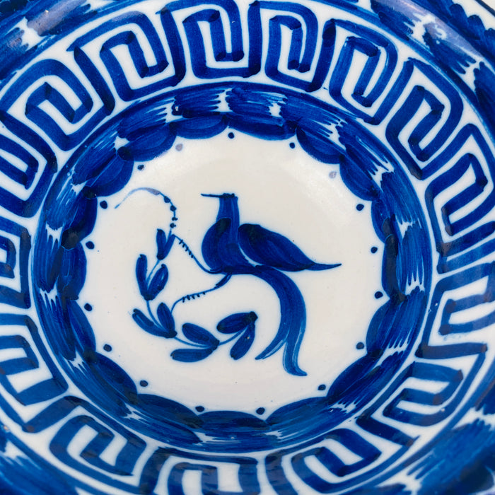 Antique Spanish Manises bowl, cobalt blue bird and botanical motif on white tin glaze, with a Greek key border that frames the interior patterning. The deep bowl form works as a decorative bowl, fruit bowl, or serving bowl for dry foods, and complements Mediterranean decor, wabi sabi decor, and French country decor without changing its Spanish ceramic identity.
