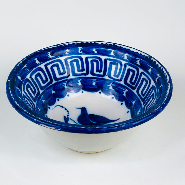 Antique Spanish Manises ceramic deep bowl in blue and white tin glazed earthenware from the Valencia region, featuring a hand painted cobalt bird in the center with a curling leafy branch. The rim is structured with a Greek key border and bold cobalt brushwork, ideal for Mediterranean decor styling and blue white kitchen decor.