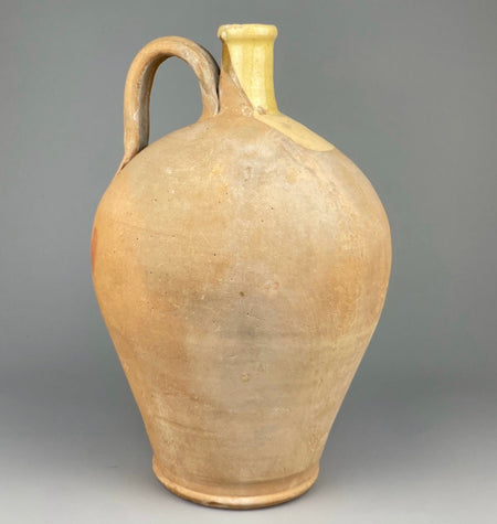Full view of antique French terracotta water jug with classic ovoid shape, curved handle, and glazed yellow neck. This early 20th-century cruche is a traditional French pottery vessel used for wine or water, perfect for Mediterranean farmhouse or rustic French country decor.