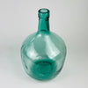 Aqua blue glass demijohn vase with a rounded body and tall neck, made as a Spanish wine carboy by V. Ayelense. The translucent blue green glass shows bubbles, moulded seams, and utilitarian production marks, while the scale and color make it useful as a floor vase, branch vase, or sculptural glass object for coastal decor.