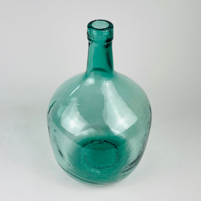 Aqua blue glass demijohn vase with a rounded body and tall neck, made as a Spanish wine carboy by V. Ayelense. The translucent blue green glass shows bubbles, moulded seams, and utilitarian production marks, while the scale and color make it useful as a floor vase, branch vase, or sculptural glass object for coastal decor.