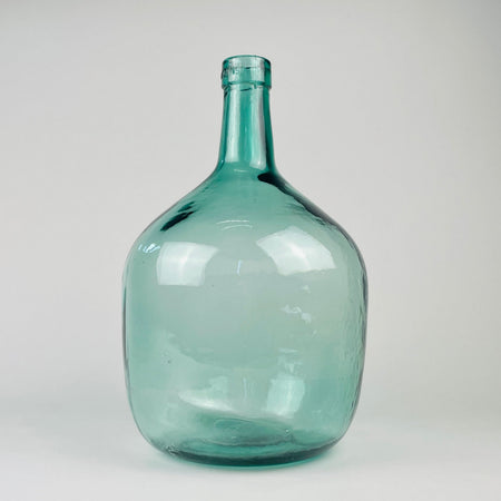 Vintage blue glass demijohn vase from Spain, marked V. Ayelense on the neck and originally made as a wine carboy or damajuana. The aqua blue green glass has a rounded body, narrow neck, visible bubbles, mould seams, and irregular surface movement, making it suitable as Mediterranean decor, coastal decor, or a large glass vase.
