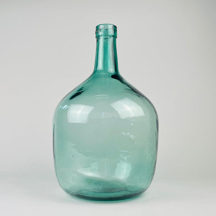 Vintage blue glass demijohn vase from Spain, marked V. Ayelense on the neck and originally made as a wine carboy or damajuana. The aqua blue green glass has a rounded body, narrow neck, visible bubbles, mould seams, and irregular surface movement, making it suitable as Mediterranean decor, coastal decor, or a large glass vase.