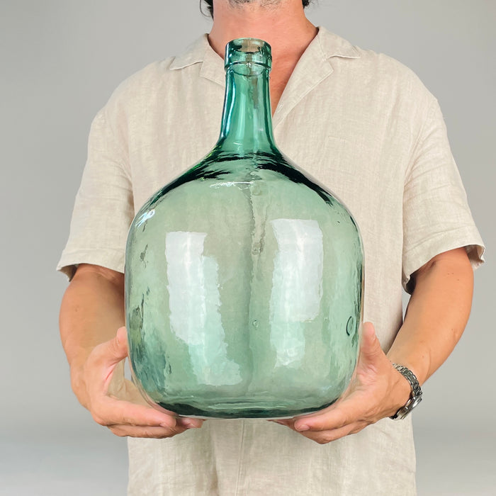 Spanish blue glass demijohn vase with raised V. Ayelense lettering around the neck, identifying it as a mid 20th century wine carboy from Aielo de Malferit, Valencia. The rounded aqua glass body, narrow neck, trapped bubbles, and handmade irregularities give it strong decorative value for vintage home decor and farmhouse decor.