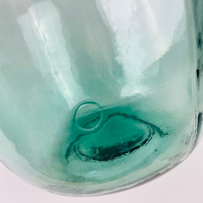 Spanish blue glass demijohn with V. Ayelense neck mark, identifying the maker on the raised collar of the bottle. The piece has a rounded wine carboy body, narrow neck, aqua blue green glass, and visible bubbles, making it a distinctive decorative vase for collectors of vintage glass and Mediterranean home decor.
