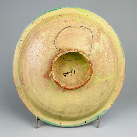 Back detail of the bowl's clay body and red foot ring, with green glaze over-spray and stamped maker's mark. This footed base adds dimension and authenticity to the vintage ceramic plate made for wall decor or shallow serving. Rear view of vintage Moroccan ceramic bowl showing unglazed terracotta base with green glaze remnants, a raised foot, and a wire hanger. This bowl is a wall-mountable decorative plate crafted in mid-20th century Fez or Safi and ideal for rustic global styling.
