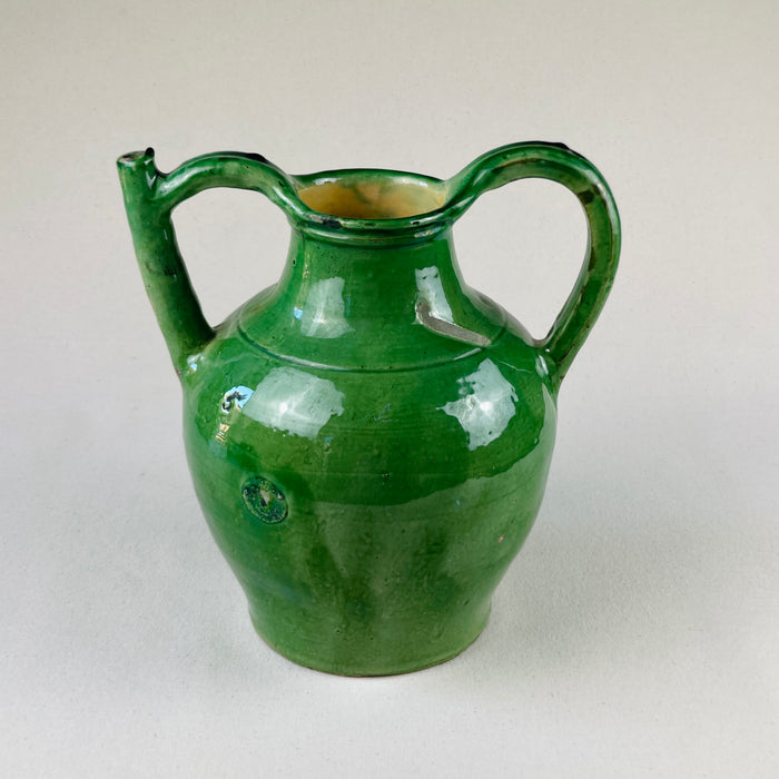 Overhead angled photo showing both handles and curvature of body for a three-dimensional effect
From a high-angle perspective, the image captures the rounded body and dual-handle design of the antique French pottery jug, emphasizing its balance, symmetry, and the tactile quality of the green glaze over the terracotta body.