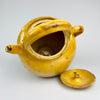 Ochre yellow French terracotta pottery water jug with the form of an antique gargoulette pot. The vessel includes a lid with small air hole, a rounded knob, a short pouring spout, and carrying handles, while the worn glaze and exposed terracotta support use as a decorative ceramic centerpiece, pottery vase, or Mediterranean decor object.