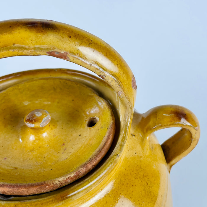Large French terracotta pottery vase formed as a yellow glazed gargoulette water jug, with an arched top handle, side spout, side loop handle, and fitted lid. The piece combines glazed and unglazed surfaces, showing exposed clay, chips, scratches, and age related patina that work well in French country decor and antique and vintage displays.