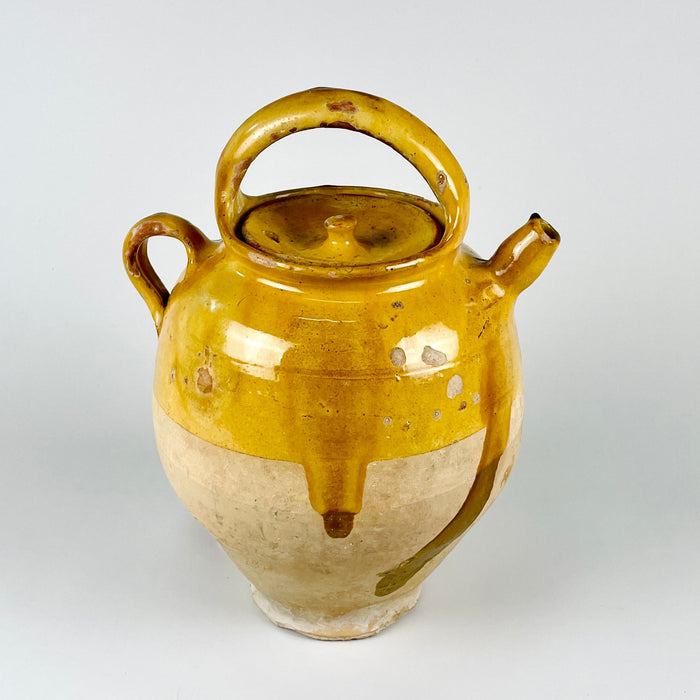 French gargoulette pot with lid in yellow glazed terracotta, showing the traditional water jug form with a filling opening, side spout, and arched carrying handle. The surface includes glaze losses, exposed earthenware, mineral flecks, darkened firing marks, and worn edges, giving the piece a strong antique folk pottery character.