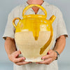 Antique French ceramic water jug in yellow glazed terracotta, with a rounded body, side spout, arched handle, loop handle, and removable lid. The pottery surface shows historic wear, glaze chips, scratches, exposed clay, and base abrasions, making it an expressive decorative vessel for antique pottery collectors and vintage home decor.