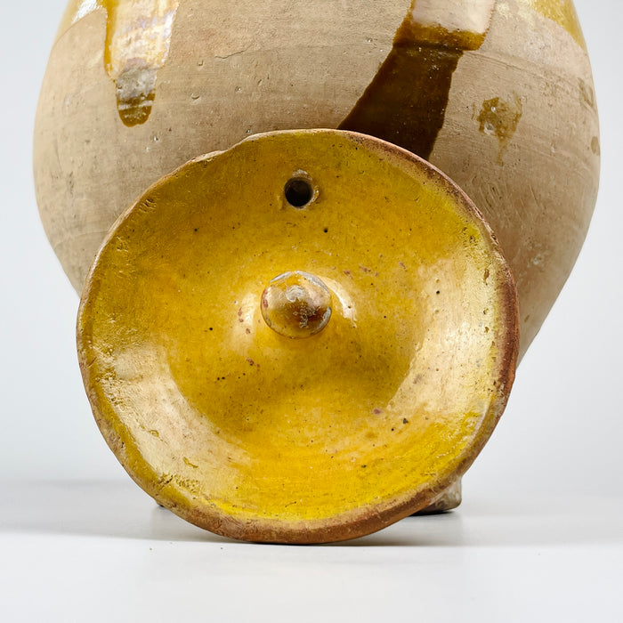 French folk pottery gargoulette jug in yellow glazed terracotta, with a removable lid, side pouring spout, side handle, and large arched handle. The unglazed lower body shows clay texture, tool marks, mineral inclusions, and staining, while the glazed upper surface has chips and patina from age and use, ideal for rustic home decor.