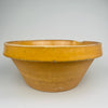 Photograph of the bowl viewed from the side angle, highlighting the rounded basin and pouring notch at the rim. These features are consistent with historic French culinary pottery once used in farmhouse kitchens. The warm amber ochre glaze adds depth and warmth, making it ideal for French country decor and rustic home decor.
