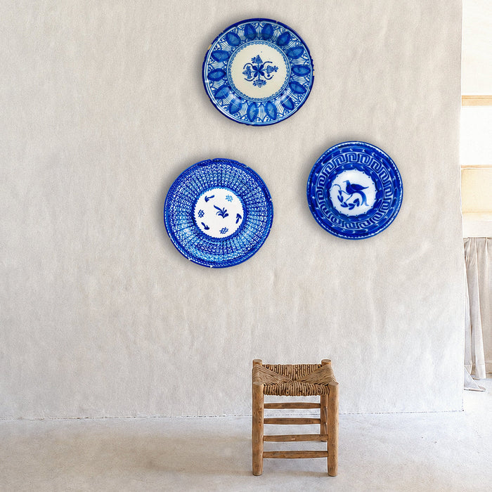 Hand painted Spanish majolica plate from Manises with deep cobalt blue decoration over a warm white glaze. The signed charger combines dense geometric repetition around the rim with looser botanical symbols at the center, producing a graphic handmade surface. Small chips and glaze losses around the edge are visible and consistent with age.