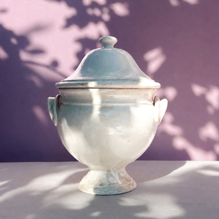 Mid Century Modern French decorative bowl in white glazed earthenware, combining a domed lid, rounded finial, twin handles, bulbous body, and flared pedestal foot. The large ceramic tureen has a softly distressed surface and sculptural silhouette for French country decor, wabi sabi decor, or Mediterranean home decor.